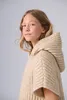 A young girl wearing a beige knitted hooded poncho. Produktbild-Vorschau