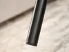 A close-up shot of the black leg of a piece of furniture, likely a table or couch, resting on a textured floor. Náhled obrázku produktu