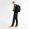 A young man wearing a jacket, t-shirt, jeans, and sneakers, carrying a black backpack. Produktbild-Vorschau