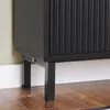 A close-up view of the bottom section of a black cabinet with fluted doors, showing its legs and the floor. Náhľad obrázku produktu