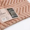 A close-up of a folded brown blanket with a chevron pattern, showing a product tag with details and an image of stacked blankets. Podgląd zdjęcia produktu
