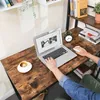 A person's hands are visible using a laptop on a wooden desk. A coffee cup and a small alarm clock are also on the desk. Podgląd zdjęcia produktu
