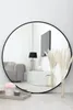 A round mirror reflecting a living room scene, with decorative items in the foreground. Produktbild-Vorschau