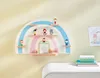 A rainbow-shaped shelf mounted on a wall, decorated with small figures and a calendar. Produktbild-Vorschau