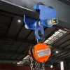 A blue trolley hoist attached to a steel beam, with an orange chain hoist hanging below it. Produktbild-Vorschau