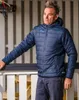 A man wearing a blue puffer jacket stands outdoors, leaning on a railing. Produktbild-Vorschau