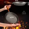A cast iron pan is shown being held by hands, with flames and sparks in the background, suggesting its use for cooking over fire. Dimensions and weight are also displayed. Produktbild-Vorschau