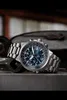 A close-up shot of a men's watch with a blue dial, resting on a metallic surface with some tools in the background. Produktbild-Vorschau