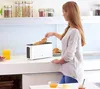A woman is putting a baguette into a white toaster on a kitchen counter. Náhled obrázku produktu