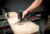 A person is using a cordless jigsaw to cut a piece of wood on a workbench. Produktbild-Vorschau