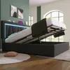 A bedroom with a bed that has its storage lifted, showing the mattress and frame. The bed has LED lighting and is in a modern setting with artwork on the wall and large windows in the background. Náhled obrázku produktu