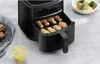 A black air fryer with chicken wings inside, next to a glass of drink and a bowl of salad. Produktbild-Vorschau