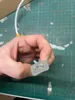 A hand holding a clear plastic electrical connector with two gold pins and a blue component inside, resting on a green cutting mat. Podgląd zdjęcia produktu