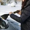 A person is using a snow brush to clear snow and ice from a car windshield. Produktbild-Vorschau