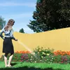 A woman watering flowers in a garden with a yellow fence in the background. Náhled obrázku produktu