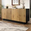 A modern sideboard with a geometric design is shown in a living room setting, placed on a rug in front of a window with blinds. Produktbild-Vorschau