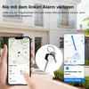 A hand holding a smartphone displaying a map application, with a set of keys and a tracker attached to them in the foreground. The background shows a house and garden. Produktbild-Vorschau