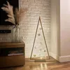 A wooden Christmas tree with LED lights and ornaments is placed on a wooden floor next to a wooden cabinet. Náhled obrázku produktu