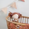 A stuffed doll and a monkey are in a crib with a fabric banner in the background. Produktbild-Vorschau