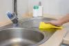A hand is cleaning a kitchen sink with a yellow sponge. Náhled obrázku produktu