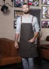 A man wearing a brown apron stands in a cafe or restaurant setting. Anteprima dell’immagine prodotto