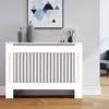 A white radiator cover with vertical gray slats is shown in a room setting, with decorative vases and a framed picture on top. Náhled obrázku produktu