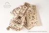 A wooden 3D puzzle model of a hurdy-gurdy is laid out on a white surface, with unassembled pieces and the brand logo visible. Produktbild-Vorschau