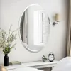 A mirror is displayed on a white wall above a white console table, with a vase of flowers and a clock on the table. Podgląd zdjęcia produktu