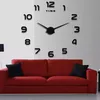 A large wall clock with loose numbers is mounted on a white wall above a red sofa with black cushions. Náhled obrázku produktu