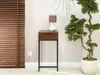 A narrow console table with a drawer and a lamp on top, placed next to wooden blinds and a large potted plant. Náhled obrázku produktu