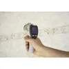 A hand holding an infrared thermometer pointed at a tiled wall. Produktbild-Vorschau