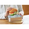 A person is holding a sandwich over an open lunchbox. Anteprima dell’immagine prodotto