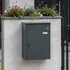 SoBuy Paketbox OGS65-DG im Regen: dunkler Metallbehälter an weißer Mauer mit Blumenoberteil Vista previa de la imagen del producto