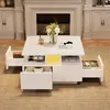 A white, high-gloss coffee table with multiple drawers and compartments is shown in a living room setting, in front of a fireplace. Podgląd zdjęcia produktu