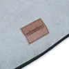 A close-up of a light gray fabric with a brown leather tag that has the brand name 'relaxdays' embossed on it. A black zipper is visible along the bottom edge. Náhľad obrázku produktu