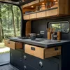 Interior of a camper van kitchen with a sink, stove, and cabinets, set against a backdrop of a forest. Anteprima dell’immagine prodotto