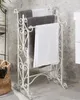 A white metal towel rack with three bars, holding three towels in a bathroom setting. Náhled obrázku produktu