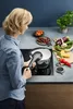 A woman is cooking with a pressure cooker on a stovetop, surrounded by fresh ingredients. Náhled obrázku produktu