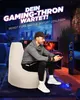 A man is playing a video game while sitting on a large beanbag chair in a dimly lit room with gaming equipment. Produktbild-Vorschau