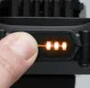 A close-up of a person's finger pressing a button on a black electronic device, with orange indicator lights showing. Produktbild-Vorschau