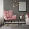 A pink rocking chair is placed in a living room setting next to a small side table with a vase and a mug. Náhled obrázku produktu