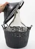 A hand is holding the lid of a black plastic basket, which contains a large glass carboy. The carboy is partially visible through the basket's lattice structure. Produktbild-Vorschau