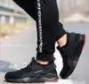 A person wearing black pants and black safety shoes with red accents, standing on a road. Produktbild-Vorschau