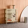 A beige metal cabinet with glass doors, displaying decorative items and books, placed against a wooden wall. Produktbild-Vorschau