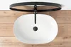 A top-down view of a white oval sink with a black faucet, mounted on a wooden surface. Anteprima dell’immagine prodotto