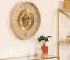 A beige and gold mechanical wall clock is displayed on a wall, with a small potted plant and a glass candle holder on a shelf below. Voir les images du produit