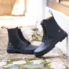 A pair of black lace-up boots are shown outdoors on a stone path. Voir les images du produit