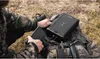 A person in camouflage clothing is using a power bank and smartphone outdoors. Produktbild-Vorschau
