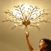 A woman is reaching up to touch a crystal on a vintage-style ceiling light fixture. Produktbild-Vorschau
