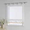 A white sheer Roman blind with a floral embroidered band and a beige linen band, hanging on a window. Produktbild-Vorschau